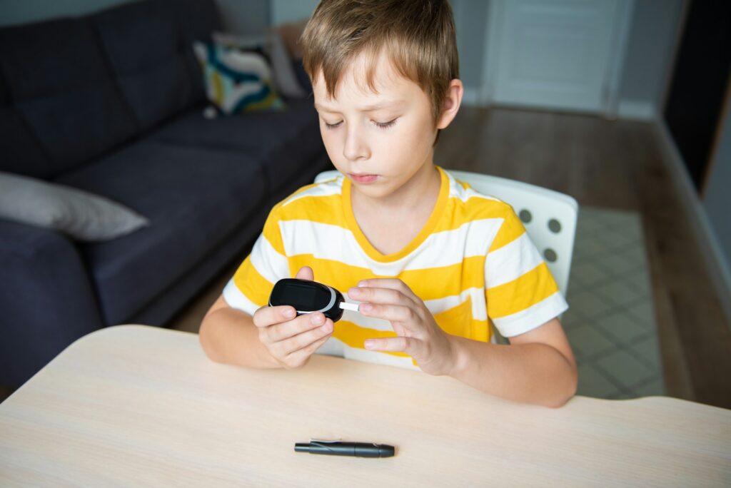 Young boy using glucometer, checking blood sugar level at home. Diabetes and children health care